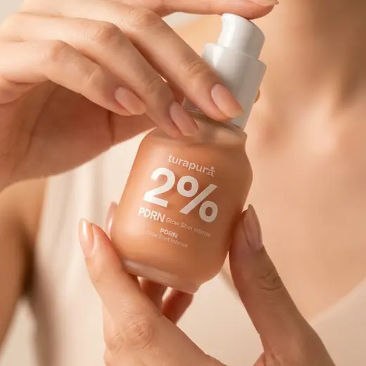 Turapura serum bottle held in hand against a peach ground, product content by Mira Visions
